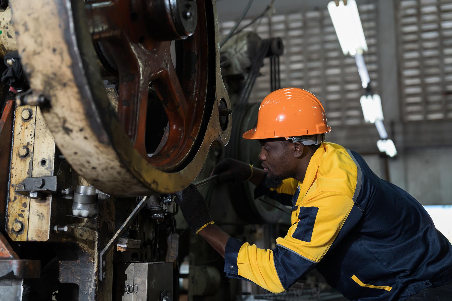 African American male engineer repairing and maintenance heavy lathe machine in industry factory. Male technician worker checking parts of lathe machine at workshop